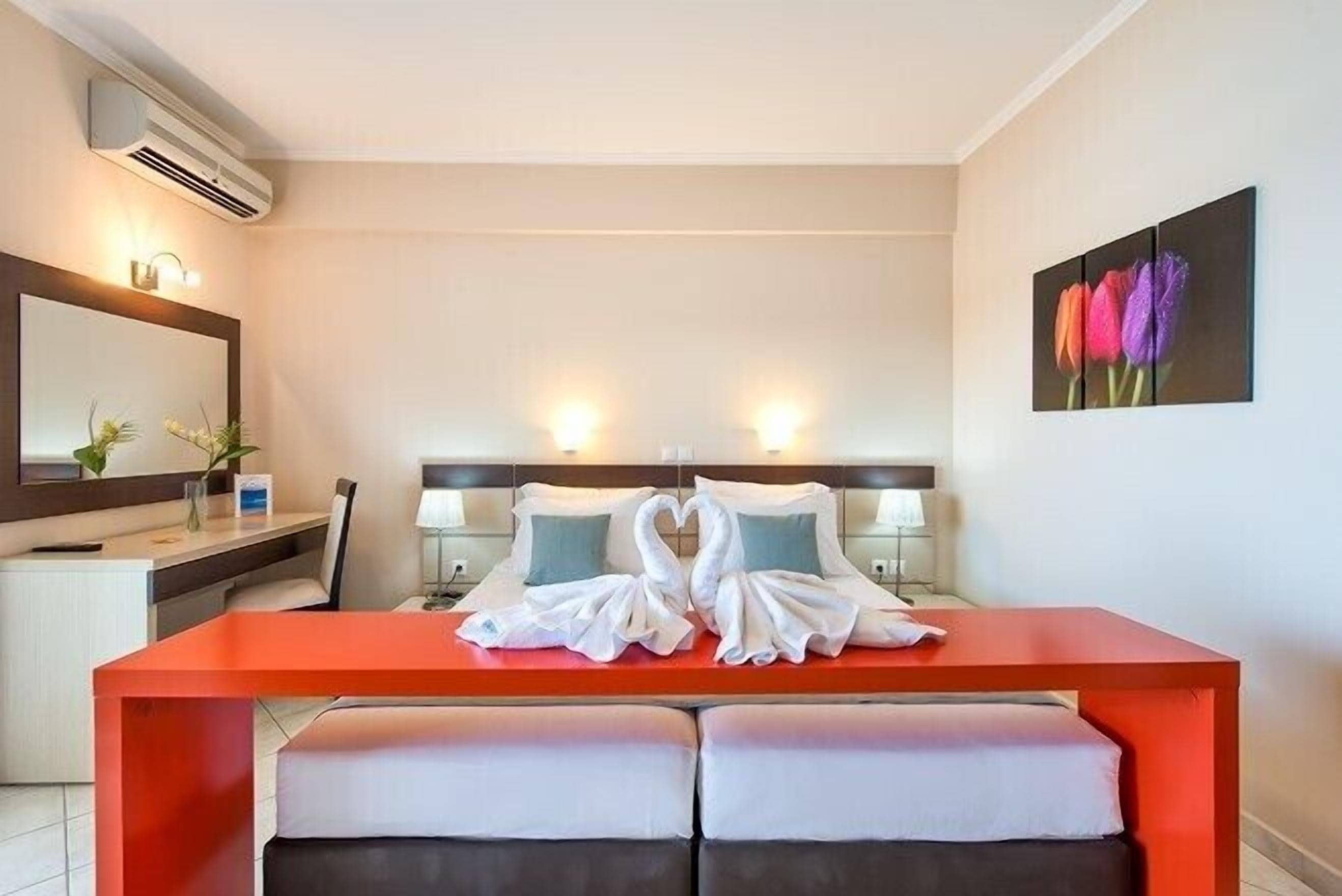 Hotelkamer met een bed, een bureau en een bankje. Er is een spiegel, een plant en een schilderij aan de muur.
