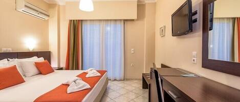 A hotel room with a bed, a desk, a TV, and an air conditioning unit.