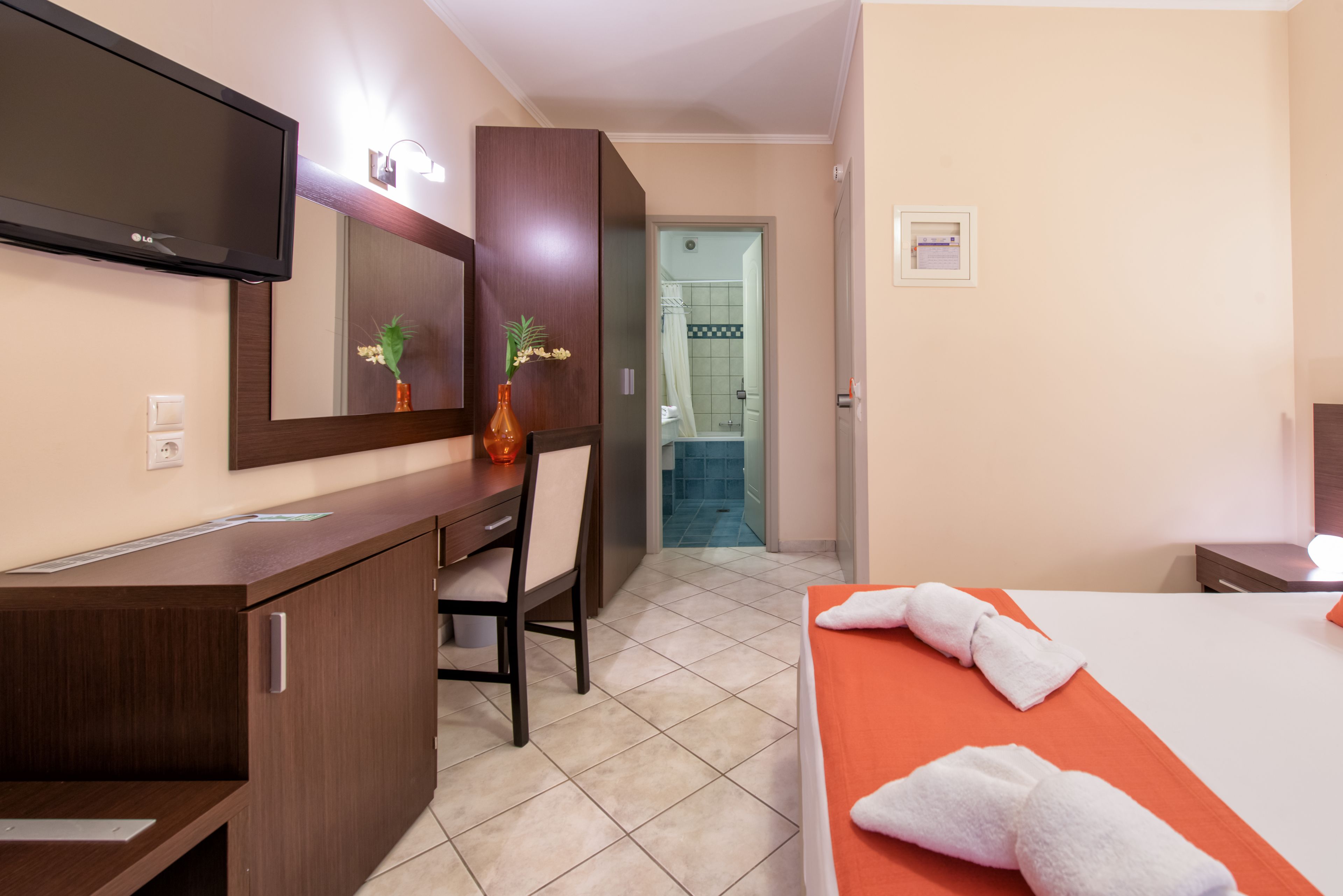 A hotel room with a bed, a desk, a chair, a TV, and a bathroom visible through an open door.