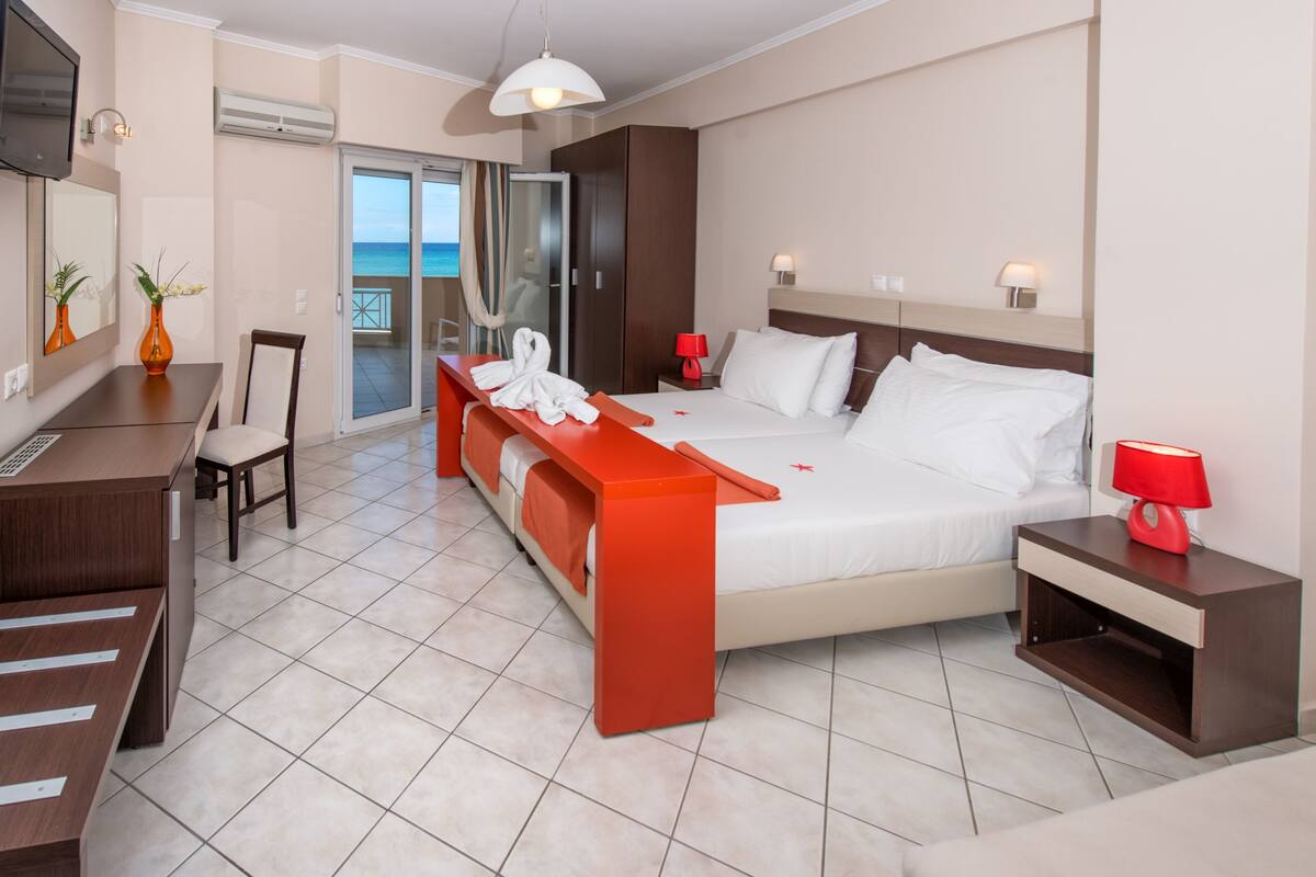 A modern hotel room with a bed, a desk, a chair, a small table, and a view of the ocean.