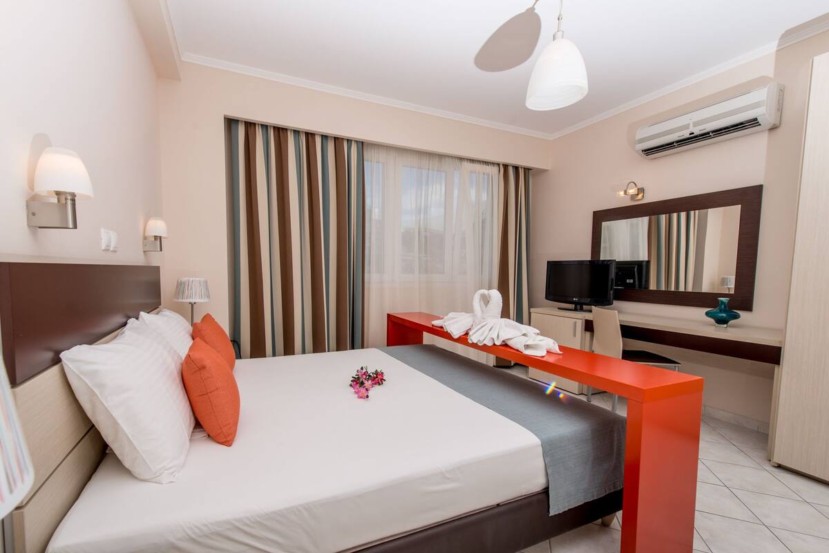A hotel room with a bed, a desk, a television, and an air conditioning unit.