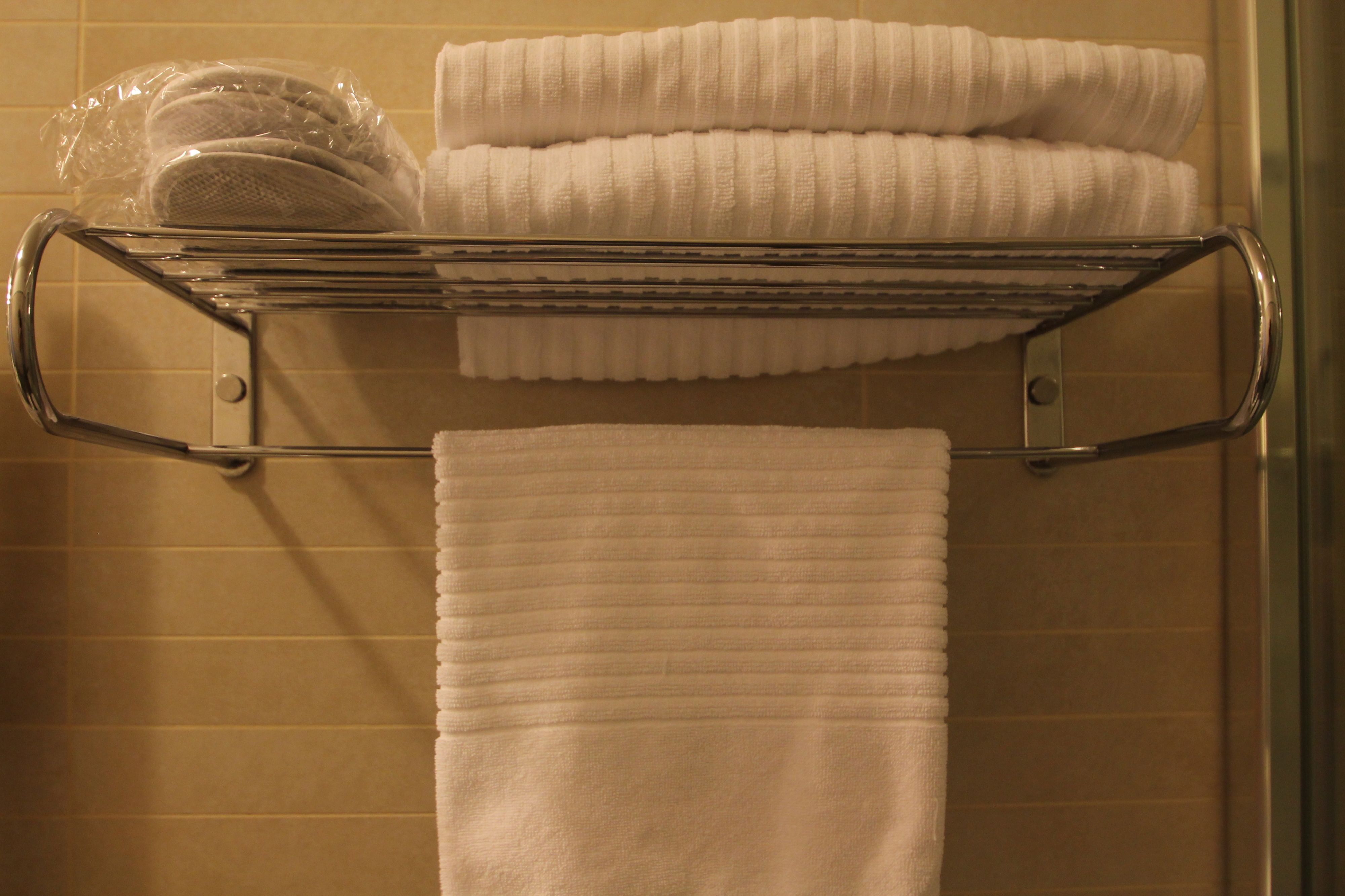 A bathroom with a towel rack holding neatly folded towels and a plastic bag.