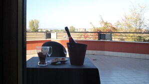 Una mesa con una botella, un vaso y un plato de comida, con vistas a un edificio y árboles.