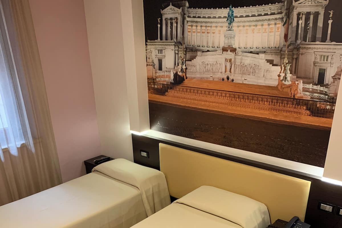 A hotel room with two single beds, a nightstand with a phone, and a large window with a view of a classical building.