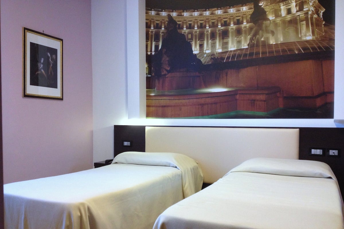 A hotel room with two single beds, a framed picture on the wall, and a large illuminated image of a building.