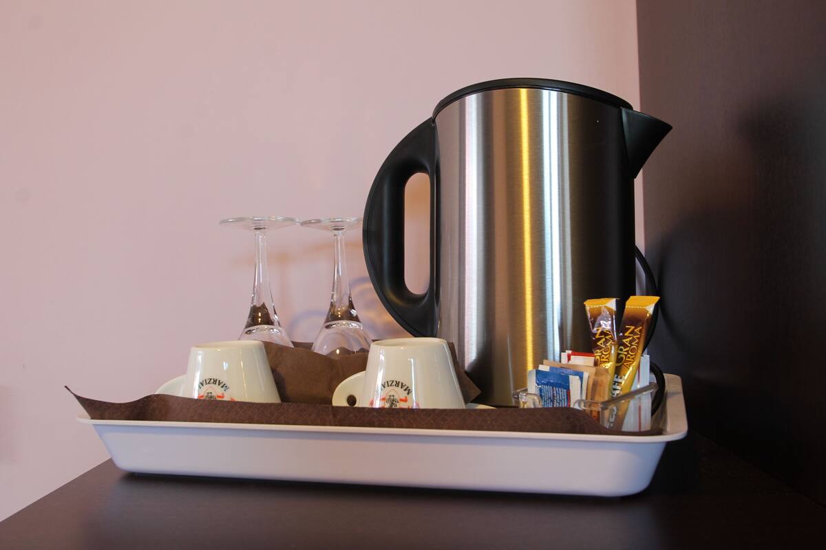 A tray with a stainless steel coffee pot, two white mugs, a glass, and some chocolate bars.