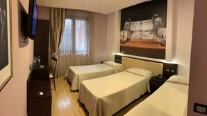 Habitación de hotel con dos camas individuales, un televisor montado en la pared, un escritorio con una silla y una ventana grande con cortinas translúcidas.