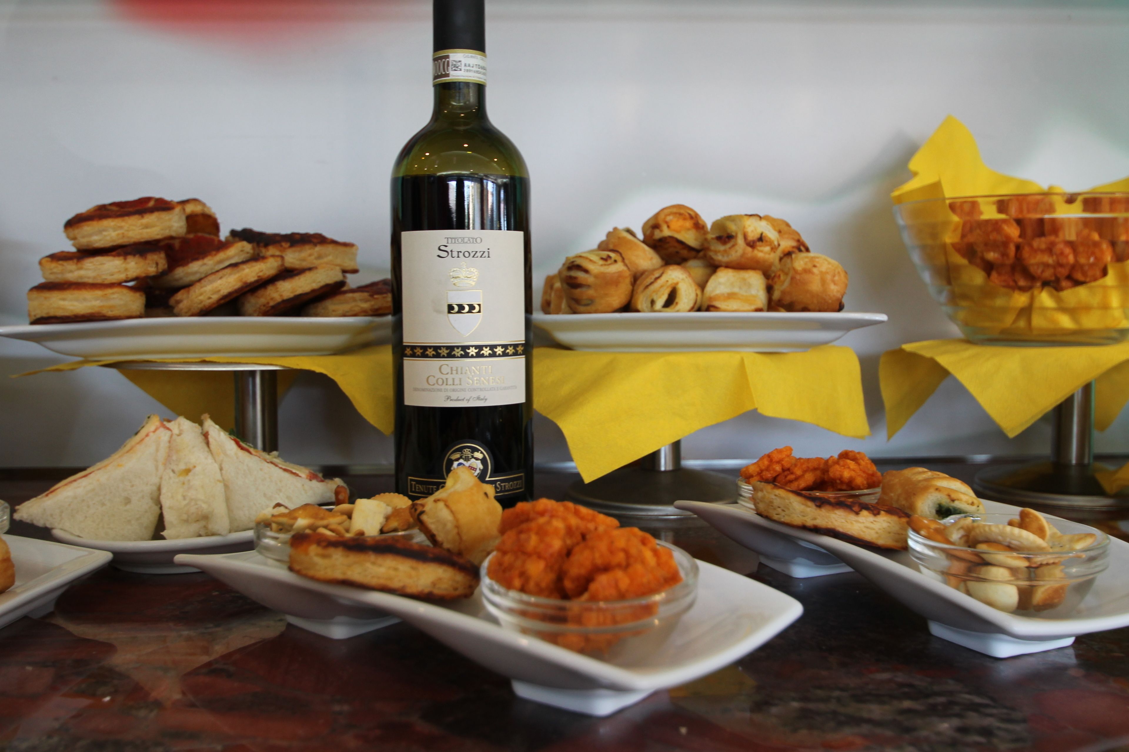 A buffet table with various dishes, a bottle of wine, and yellow tablecloths.