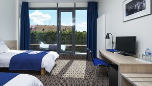 Une chambre d’hôtel avec deux lits, un bureau avec un ordinateur, une télévision et une vue sur le paysage urbain grâce à de grandes fenêtres.