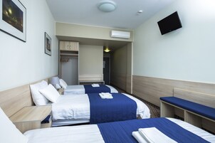 Habitación de hotel con dos camas, un televisor montado en la pared y un armario.