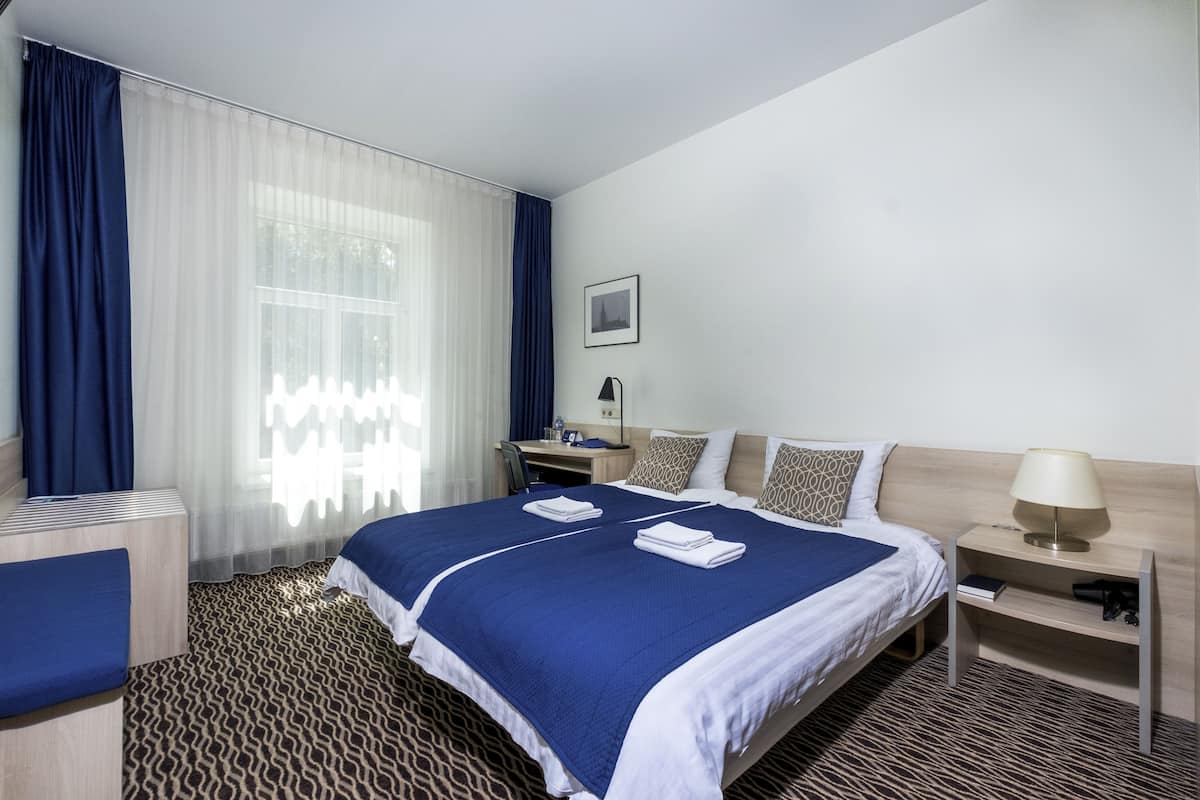 Habitación de hotel con una cama grande, un escritorio, una silla, una mesita de noche y una ventana con cortinas.