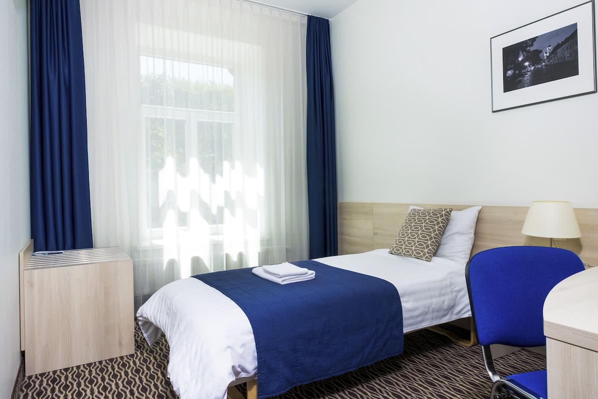 Una habitación de hotel con cama, escritorio, silla, televisor y ventana con cortinas.