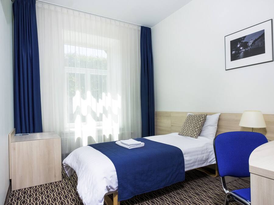 Une chambre d’hôtel avec un lit, un bureau, une chaise, une télévision et une fenêtre avec des rideaux.