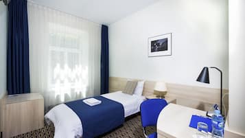 A hotel room with a bed, a desk, a chair, a nightstand, a lamp, a picture on the wall, and a window with curtains.
