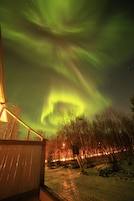Um edifício com um deque de madeira e vista para o céu noturno com a aurora boreal.