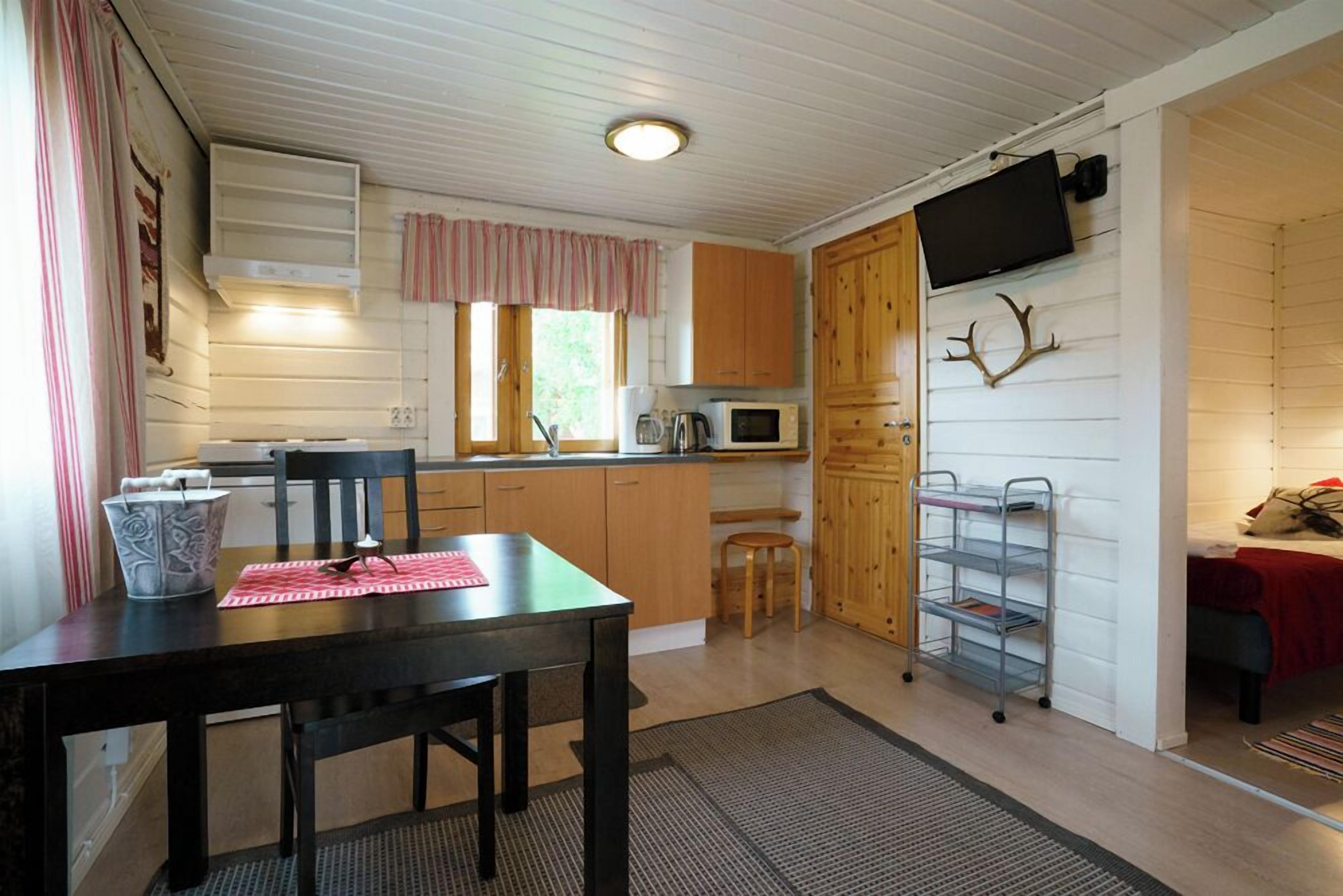 A compact kitchen with wooden cabinets, a microwave, and a television mounted on the wall.