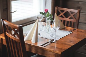 Ein Holztisch mit einer weißen Tischmatte, einer Vase mit einer rosa Rose und klarem Glasgeschirr.