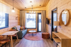 Interior acolhedor de uma cabana com teto de madeira, um sofá, uma mesa redonda, um espelho e vista para o exterior.