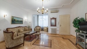 Un amplio salón con piso de parquete de madera, un sofá grande, una mesa de centro y un televisor sobre un mueble.