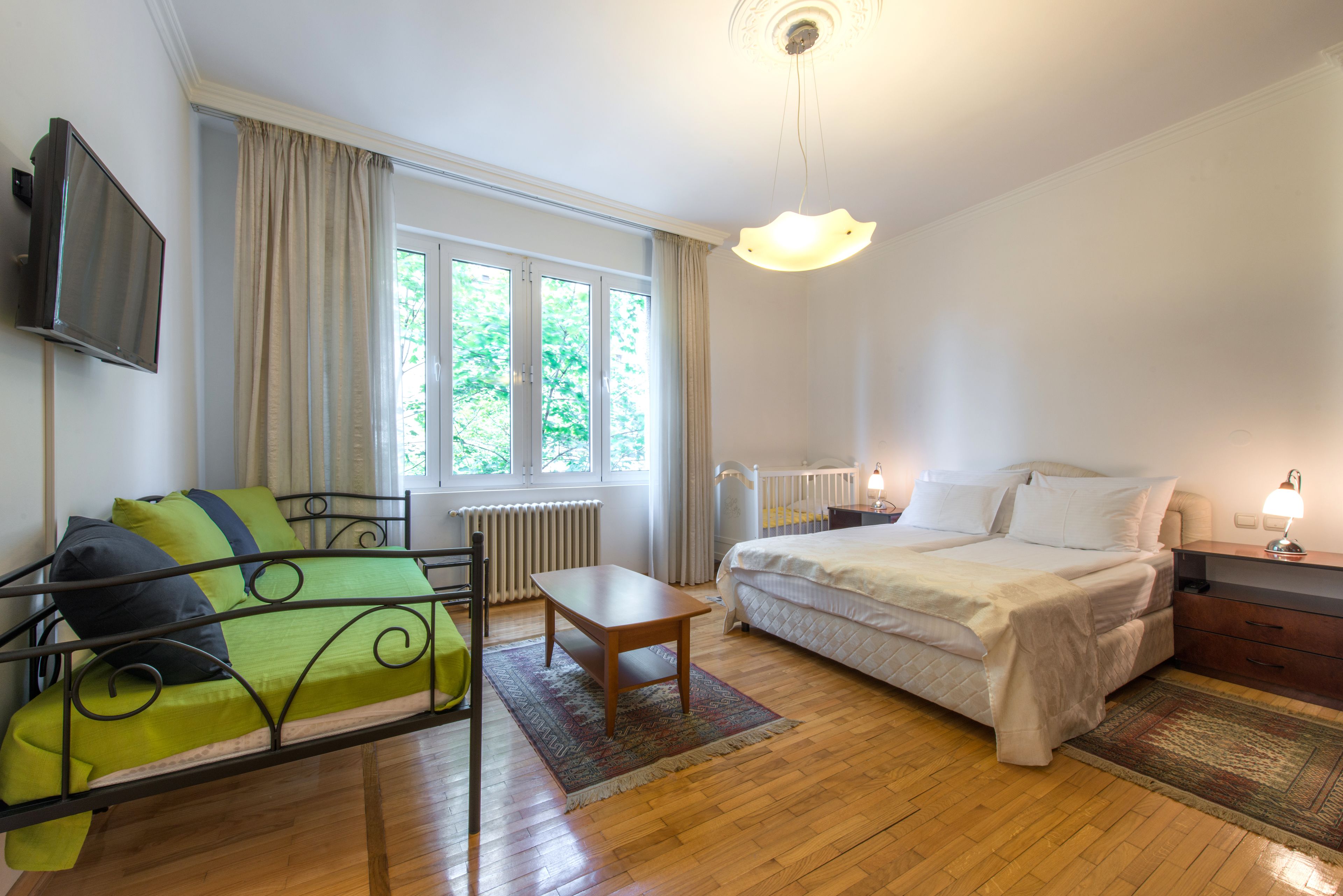 A bedroom with a bed, a sofa, a small table, a TV, and a window with curtains.