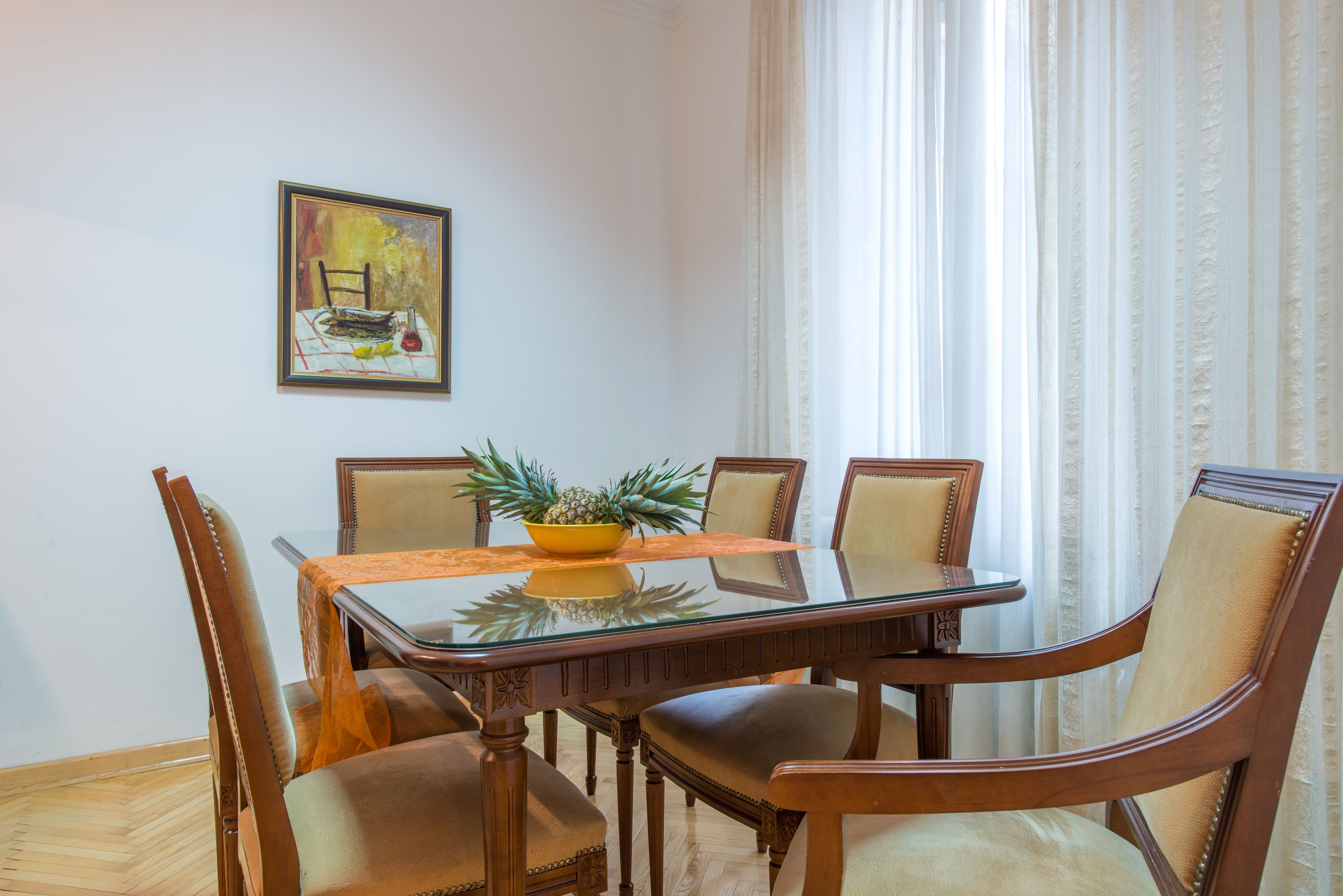 Een eethoek met een tafel met glazen blad, houten stoelen en een ananas als decoratie.