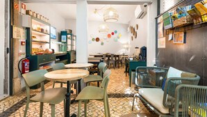 A cozy cafe with round tables and wicker chairs, a coffee machine, and shelves with jars and books. - Casa do Bairro by Shiadu (Lisbon)