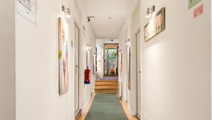 A hallway with a green carpet, white walls, and doors on both sides. There are framed artworks on the walls and a fire extinguisher mounted on the wall. - Casa do Bairro by Shiadu (Lisbon)