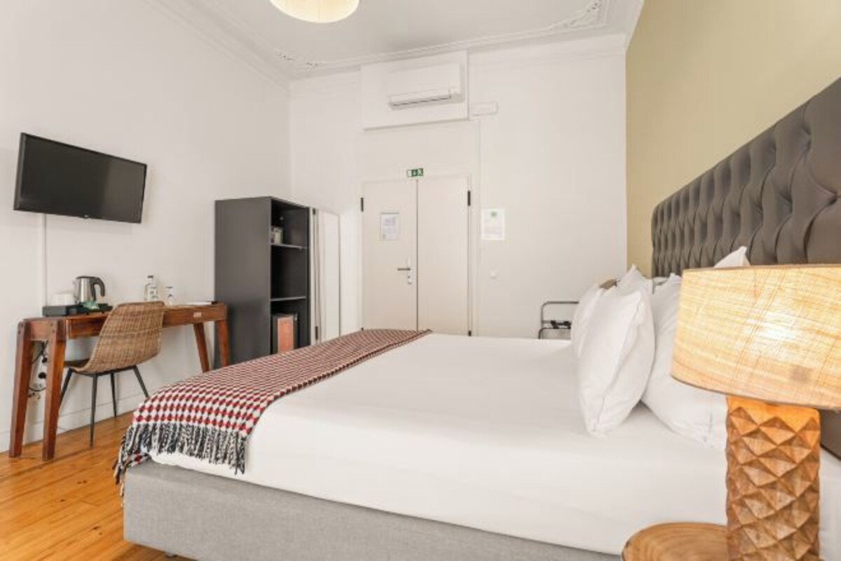 A hotel room with a bed, a desk with a chair, a television, and a wardrobe.