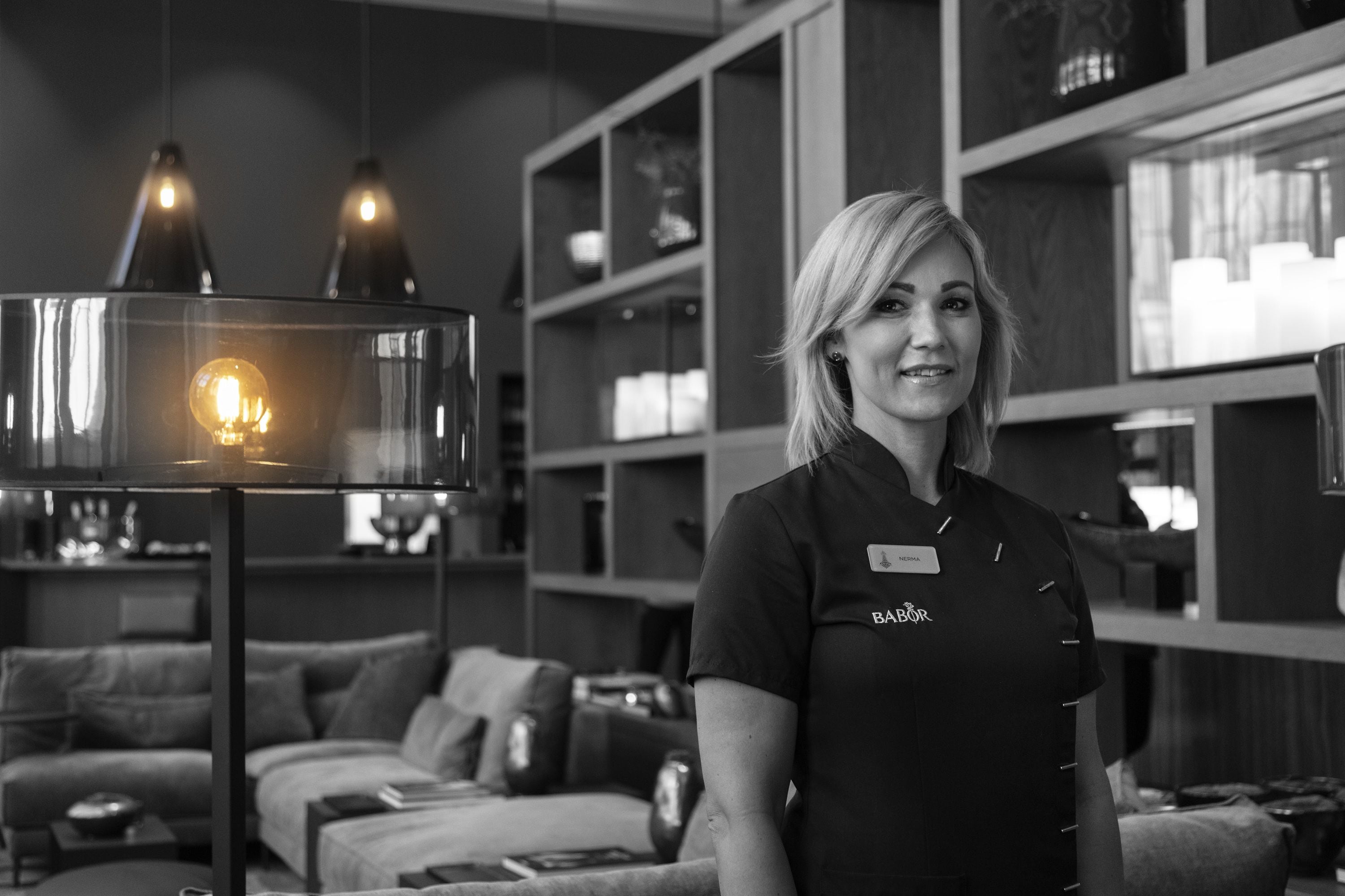 En kvinde i uniform står i et moderne, godt oplyst rum med en sofa og reoler i baggrunden.