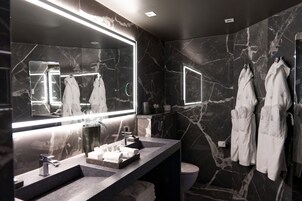 Un baño moderno con salpicadero de mármol, un espejo grande, un lavabo con mueble y dos batas blancas colgadas de ganchos.