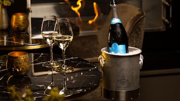 Una botella de champán en un cubo de metal con dos copas de vino sobre una mesa de mármol, sobre un fondo oscuro con una chimenea.