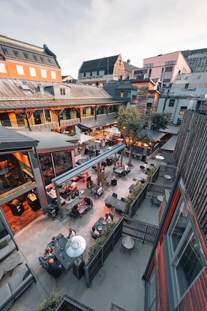 An outdoor dining area with multiple tables and chairs, surrounded by buildings with various architectural styles.
