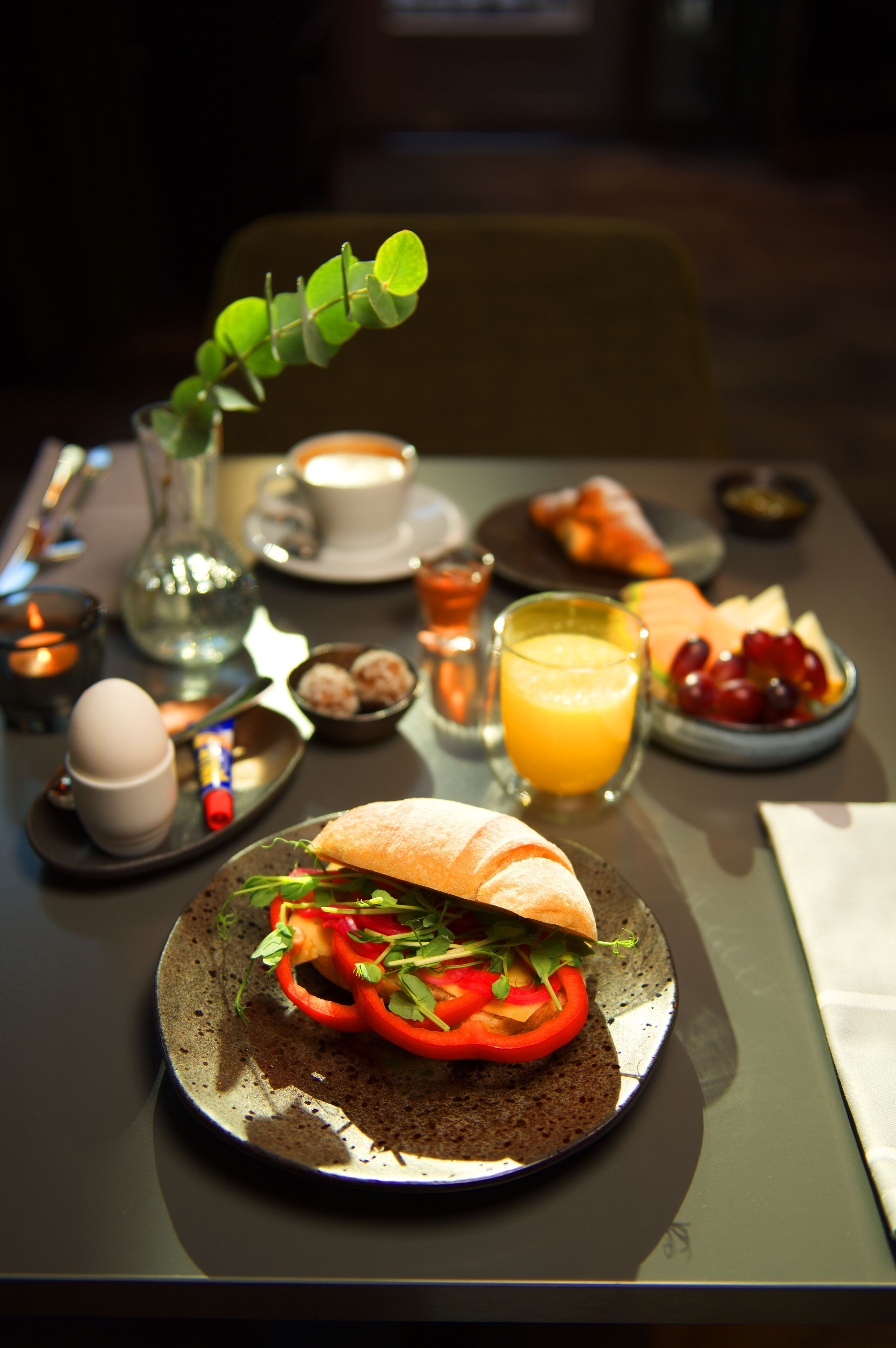 En frukostuppläggning med en smörgås, frukt och en kopp kaffe på ett bord.