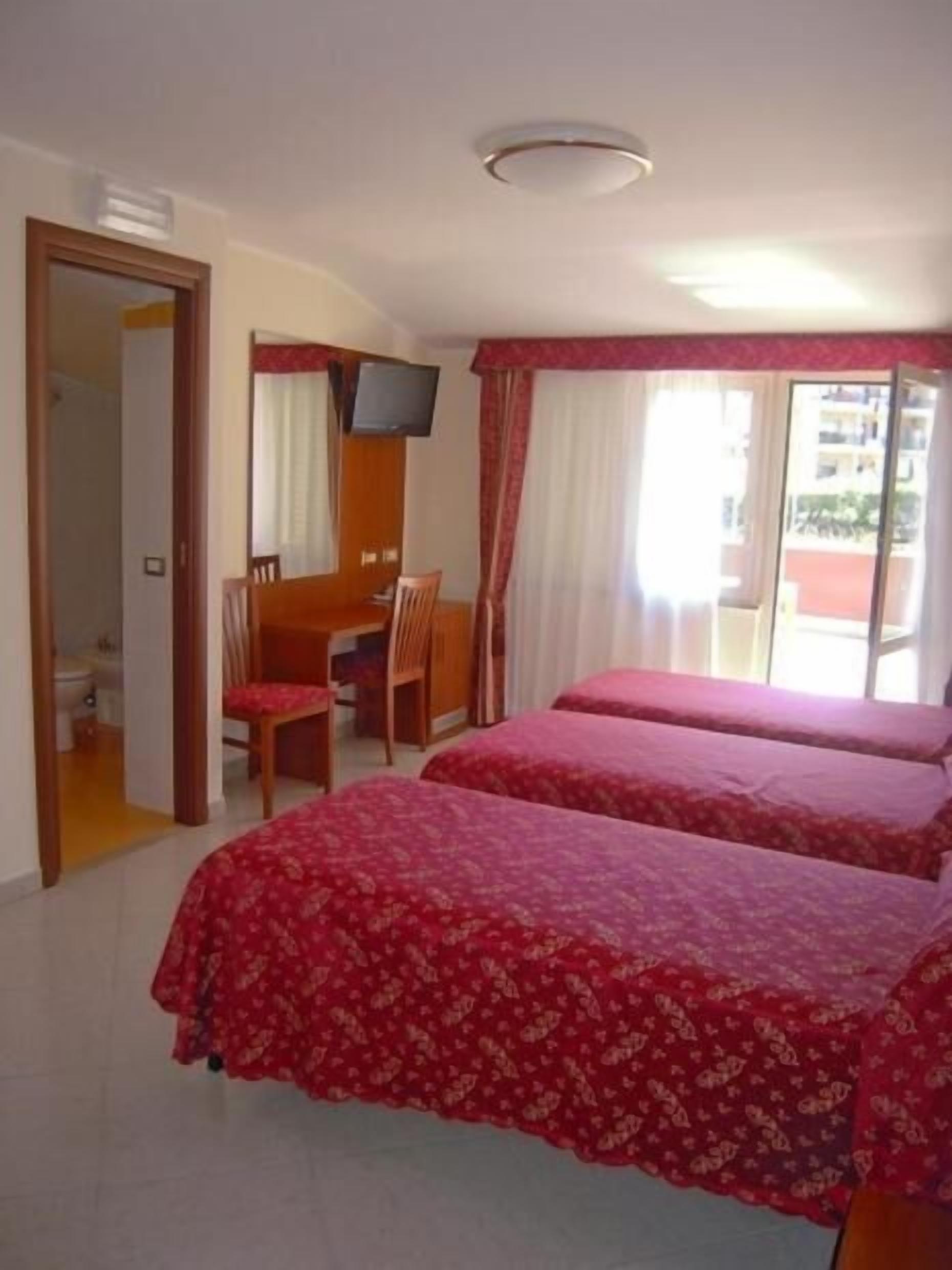 A hotel room with two beds, a desk with a chair, a television, and a bathroom visible through an open door.