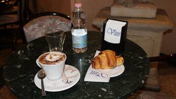 A table with a cup of coffee, a bottle of water, a croissant, and a menu.