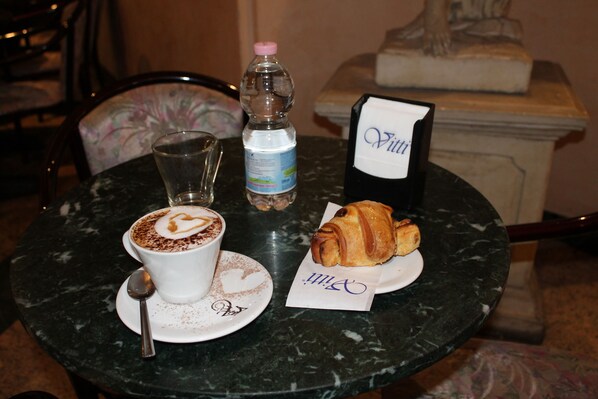 A table with a cup of coffee, a bottle of water, a croissant, and a menu.