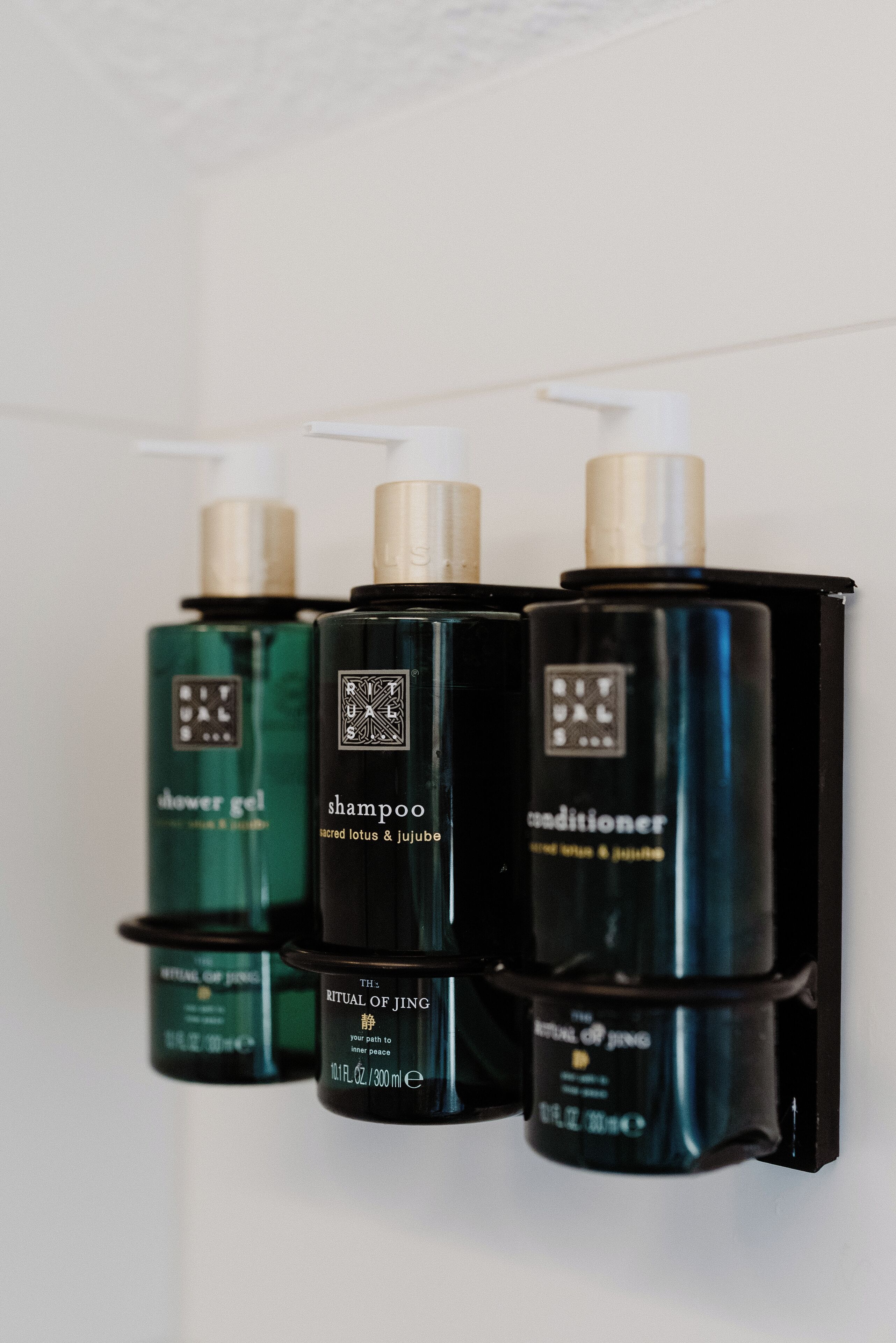 Three bottles of The Ritual of Jing hair care products on a wall.