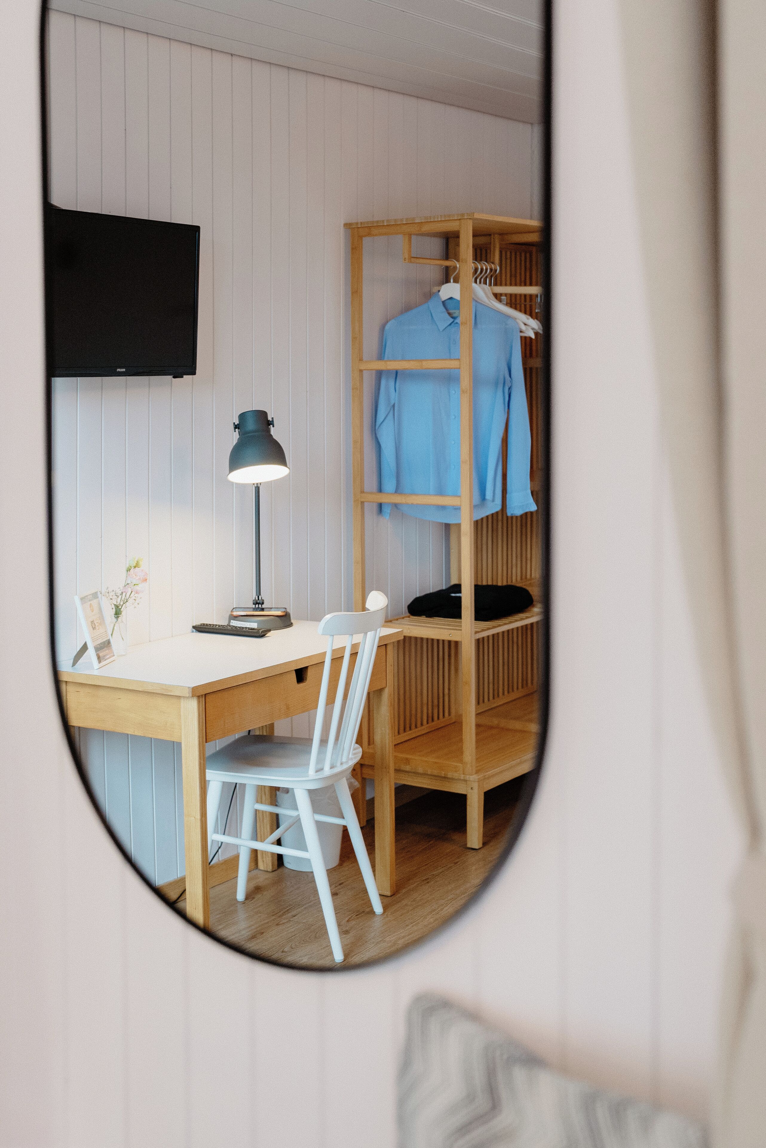 Una habitación con escritorio, silla y estante colgante con ropa.