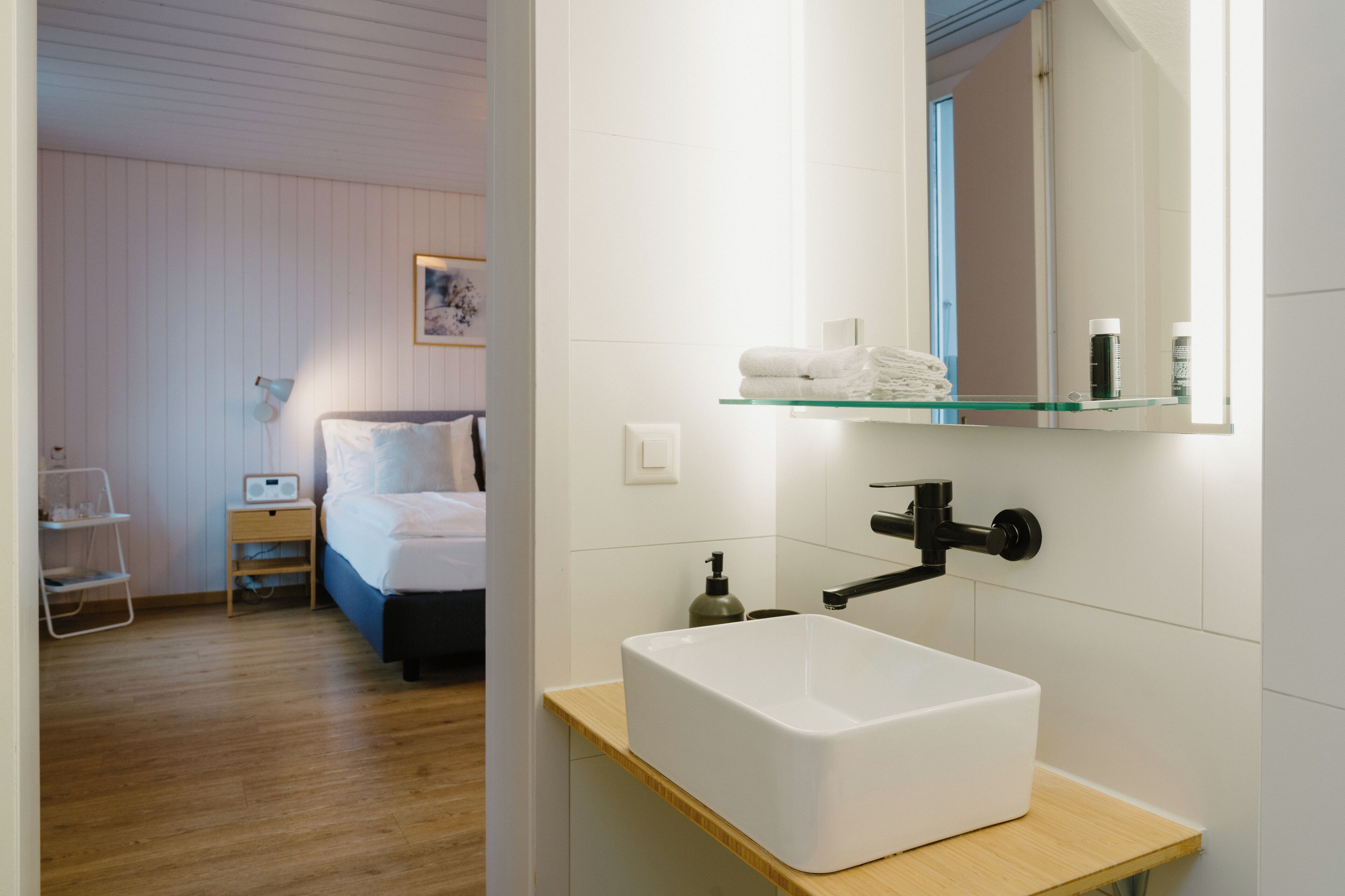 Ein modernes Badezimmer mit einem weißen Waschbecken, einer Glasablage darüber und einem Spiegel.