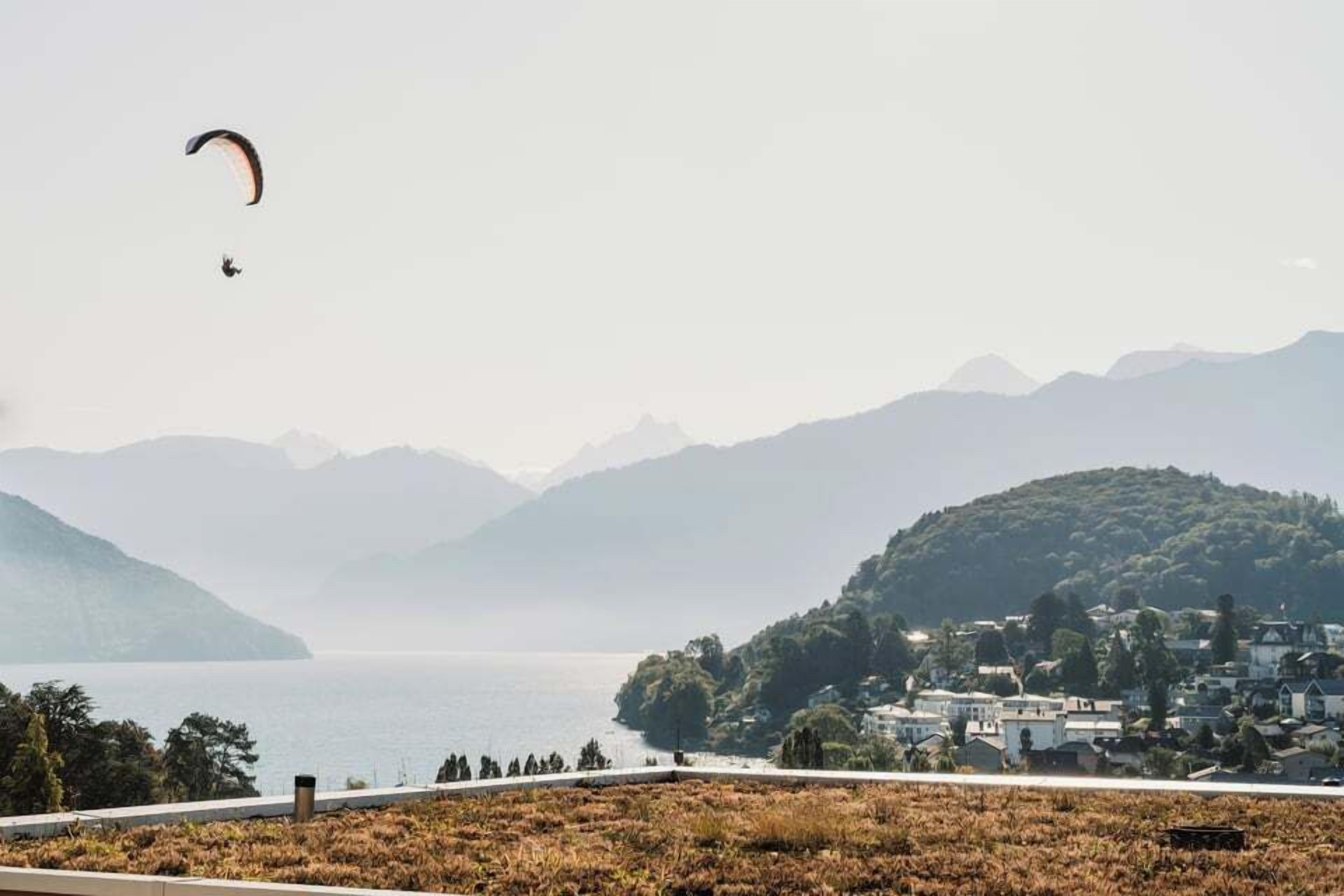 Un paysage côtier avec une personne pratiquant le parapente, une étendue d’eau et un village perché sur une colline.
