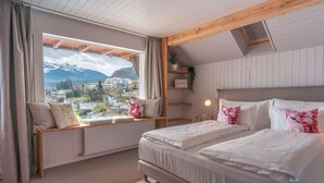 A bedroom with a large window, a bed, a bedside table, and a shelf with a plant. - La belle vue - Boutique Hotel & Café (Spiez)