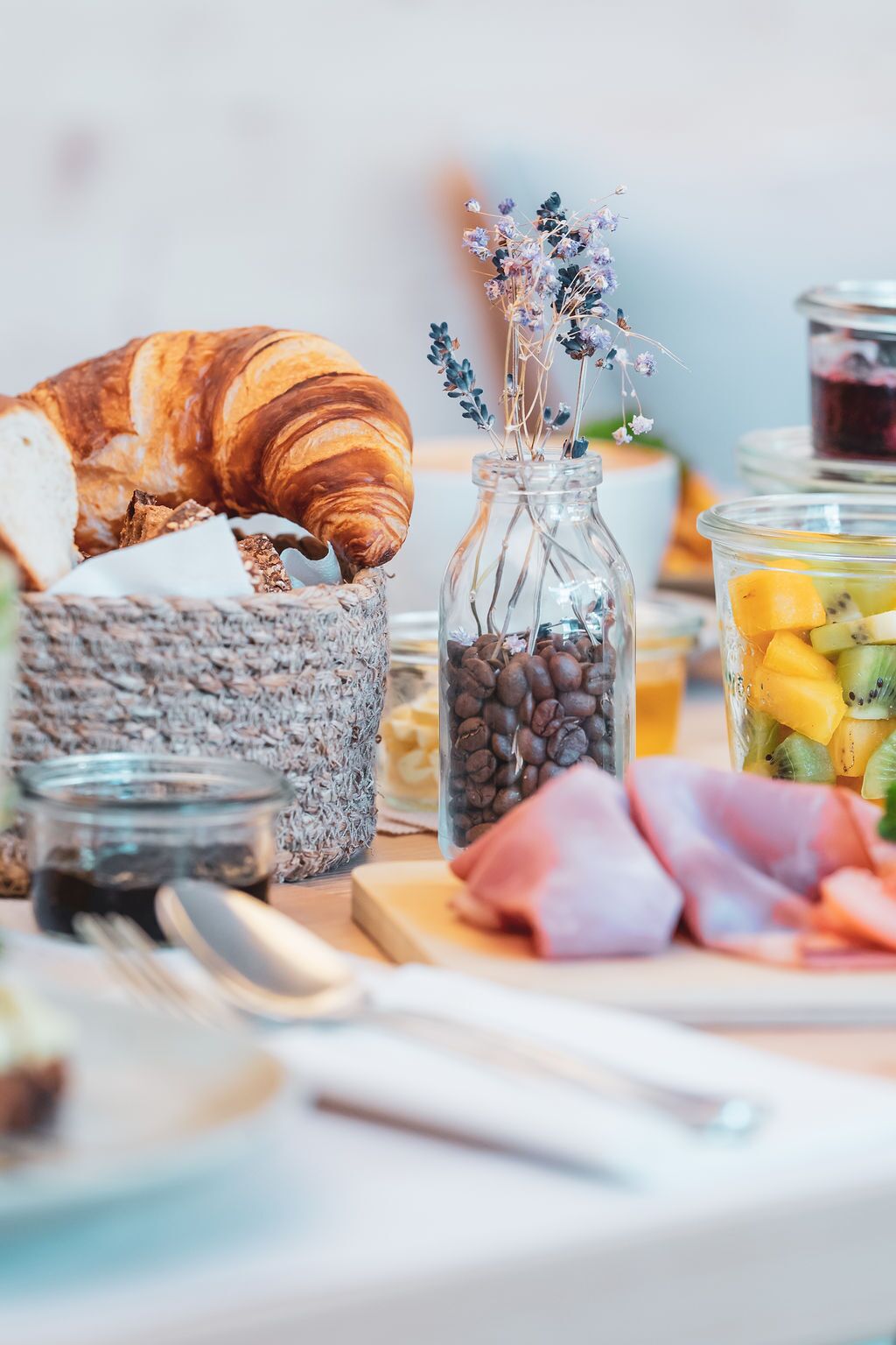 Una colazione con un croissant, un vasetto di chicchi di caffè, un bicchiere di frutta e una crema spalmabile di formaggio.