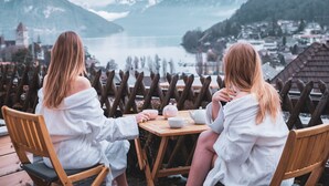 Two people seated at a wooden table with a view of a lake and mountains in the background. - La belle vue - Boutique Hotel & Café (Spiez)