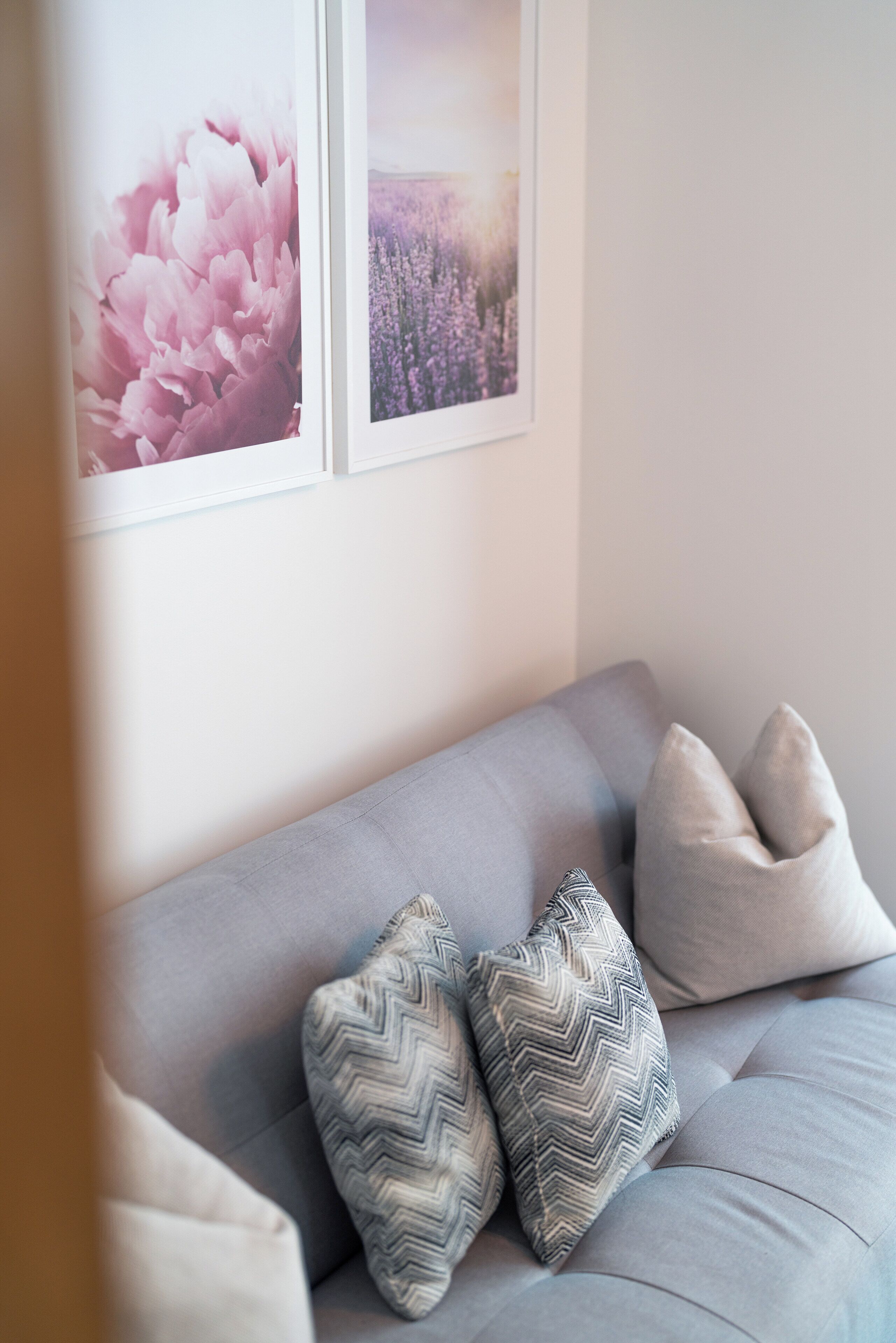 Un sofá gris con dos cojines estampados y un cuadro floral enmarcado encima.
