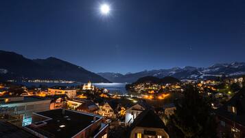 Vista nocturna de un pueblo con edificios, un lago y montañas al fondo.