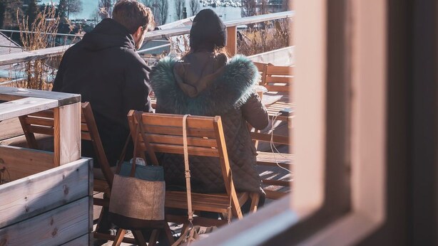 A couple and a child sitting on wooden chairs facing a lake with mountains in the background. - La belle vue - Boutique Hotel & Café (Spiez)