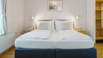 A neatly made double bed with white linens, two bedside tables with lamps, a framed picture on the wall, and a wooden bookshelf.