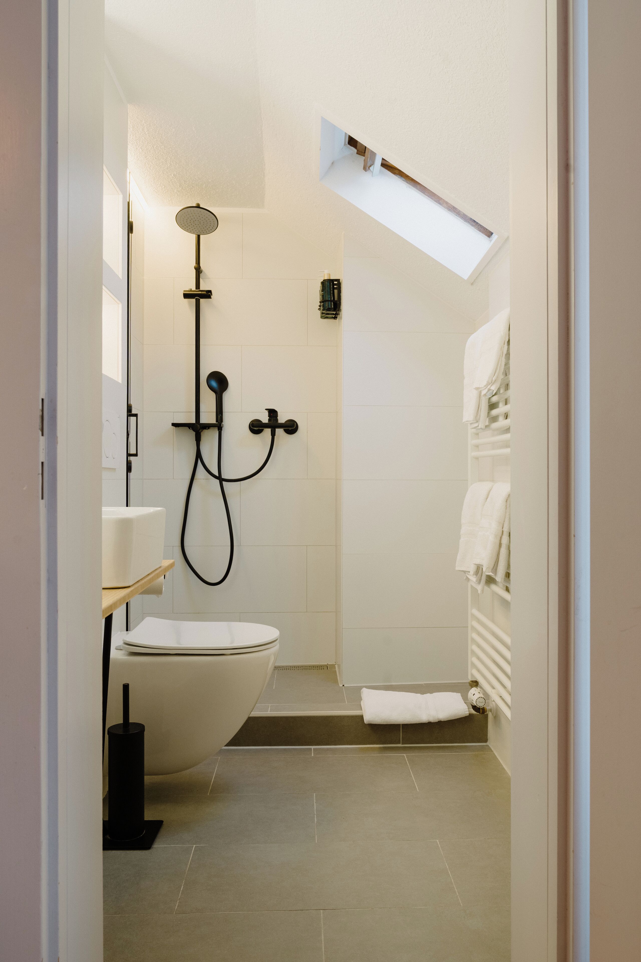 A modern bathroom with a toilet, a shower, and a towel rack.