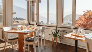 A dining area with a wooden table, white chairs, and a view of mountains and a lake. - La belle vue - Boutique Hotel & Café (Spiez)