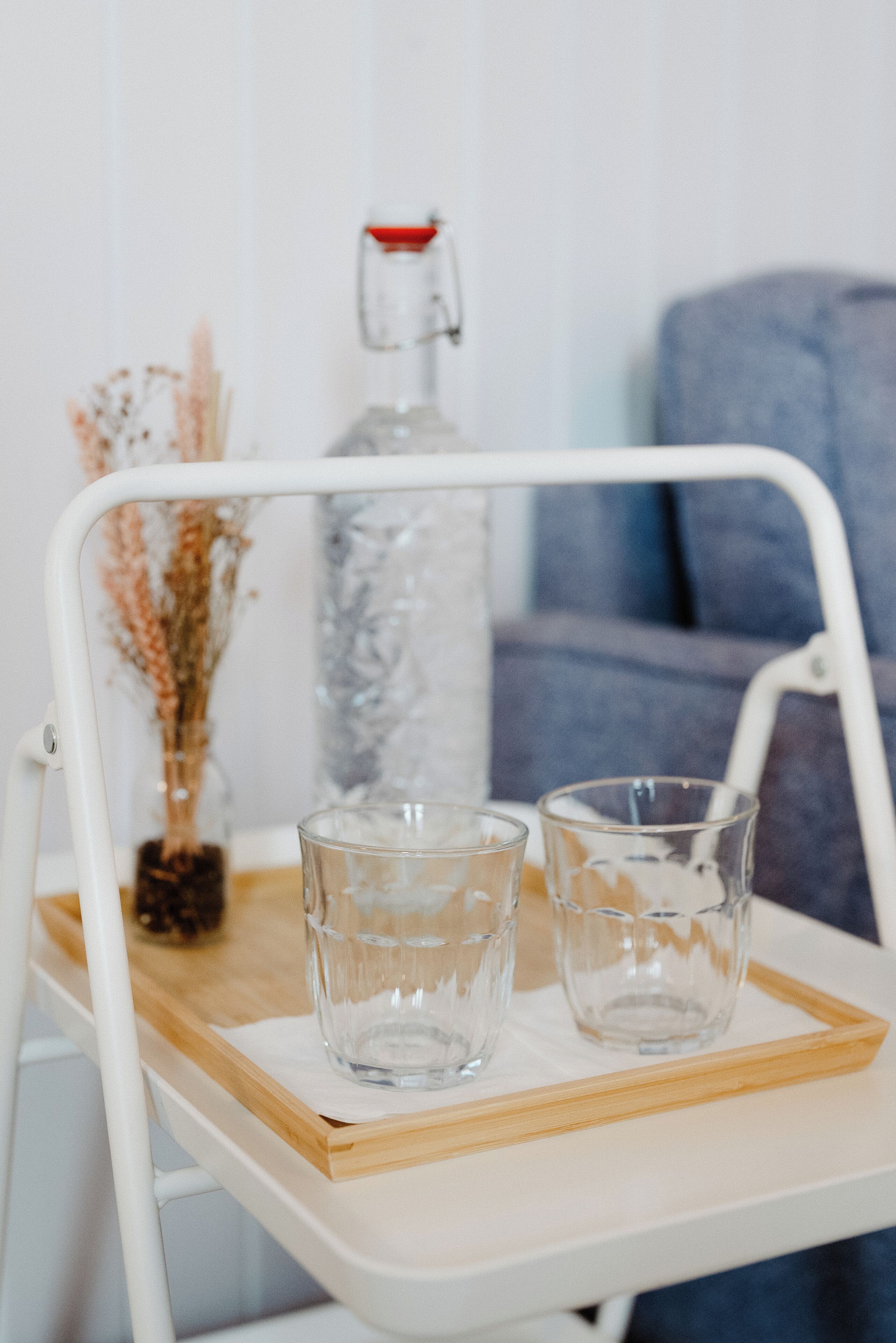 En hvid metalstol med et bakkej der holder to glas og en flaske.